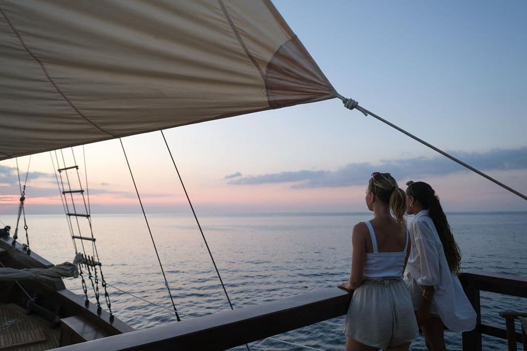 two women stand at upper deck, white sail