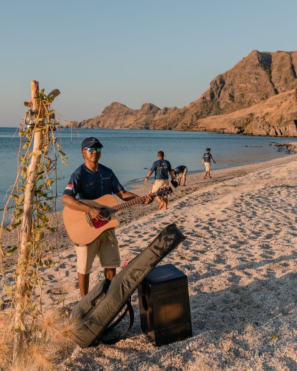 a man play guitar on beach, other men clean the beach on the background