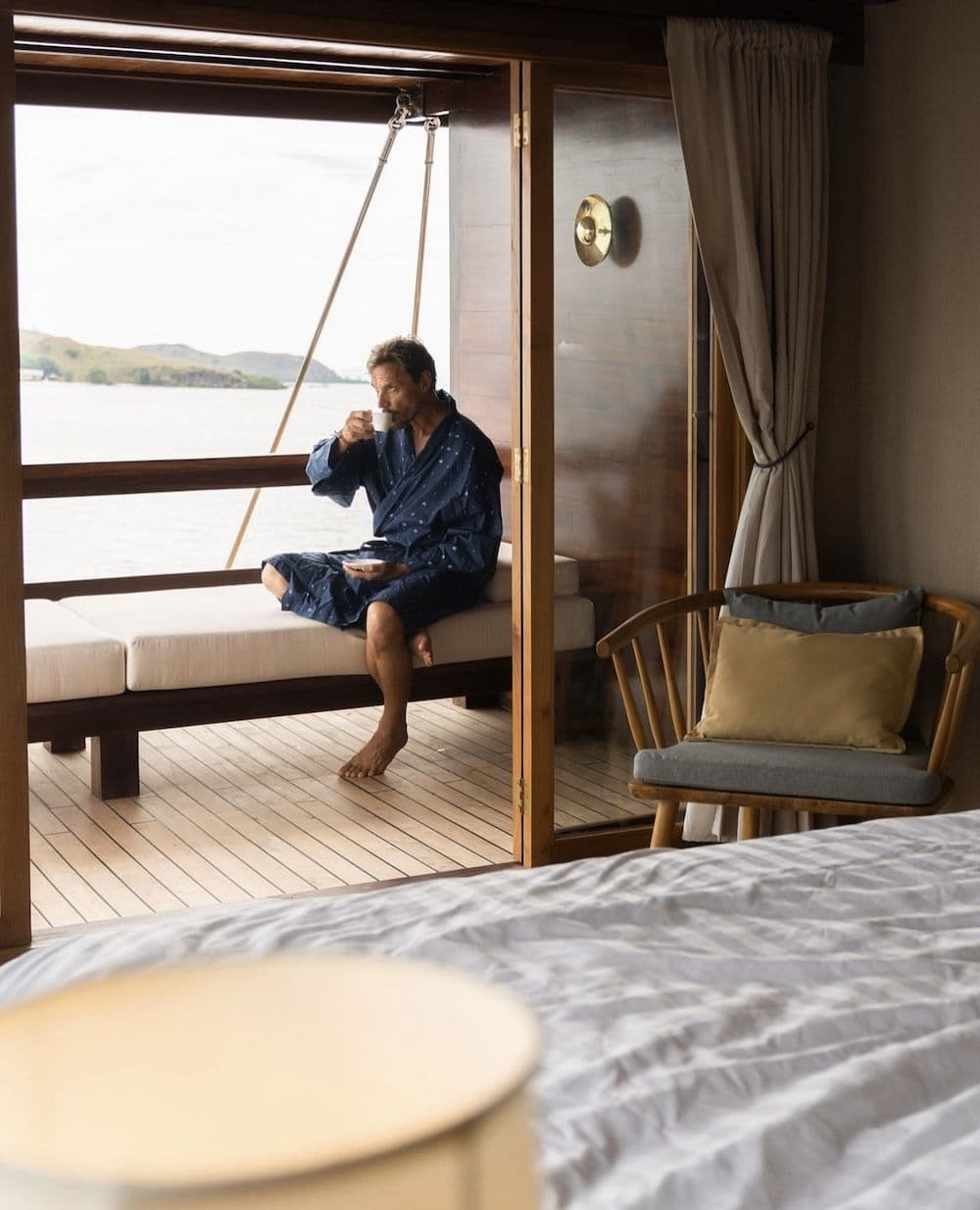 a man sit on the deck of the stateroom, blue robe, wooden chair on the corner